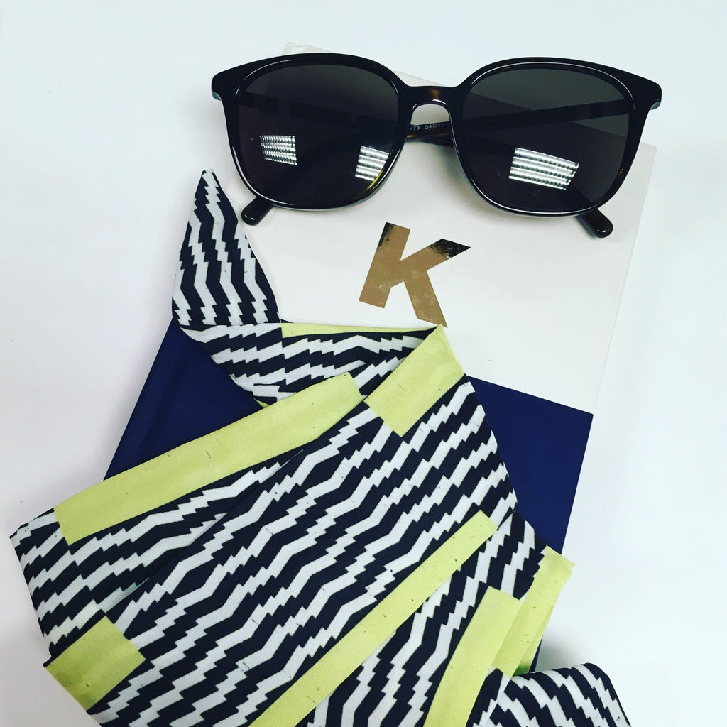 A black, white and neon yellow satin crepe scarf, styled with a notebook and sunglasses on a white background