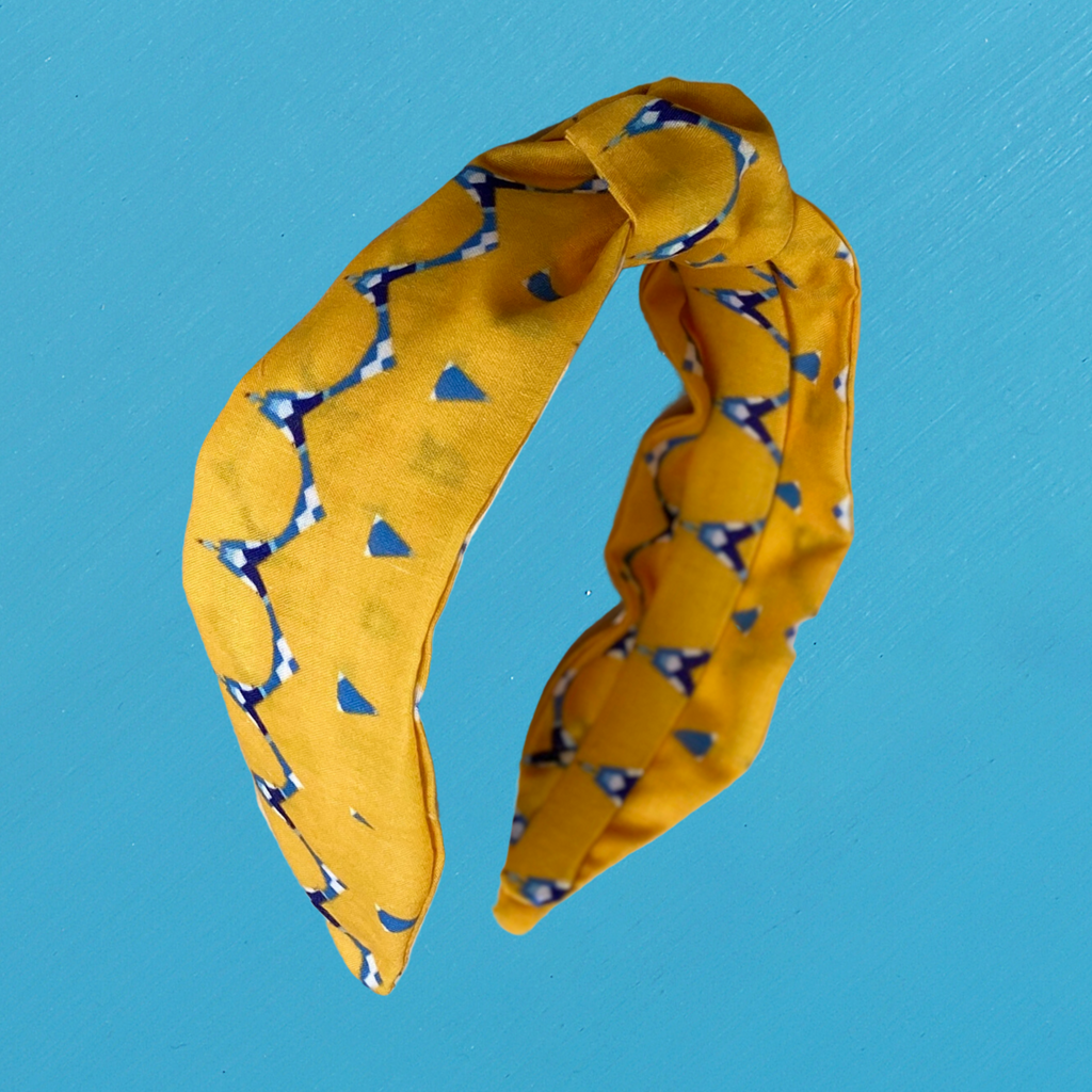 A Kate Whyley wide, knotted headband with a yellow, blue and white and pattern, called Holding Hands, on a blue background