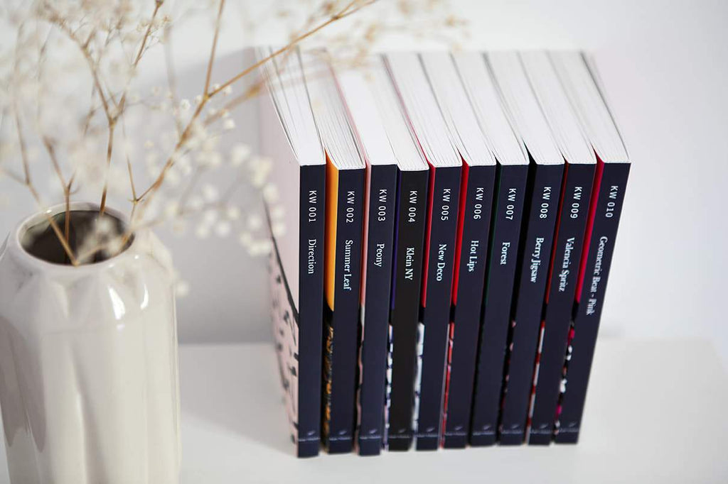 The full Kate Whyley journals range on a bookshelf, styled with white flowers in a white vase  