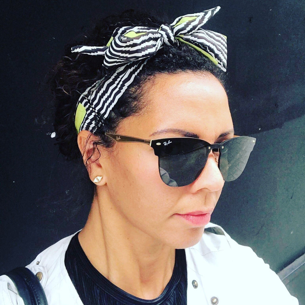 Woman wearing a black, white and neon yellow satin crepe scarf, tied in a bow around her head.