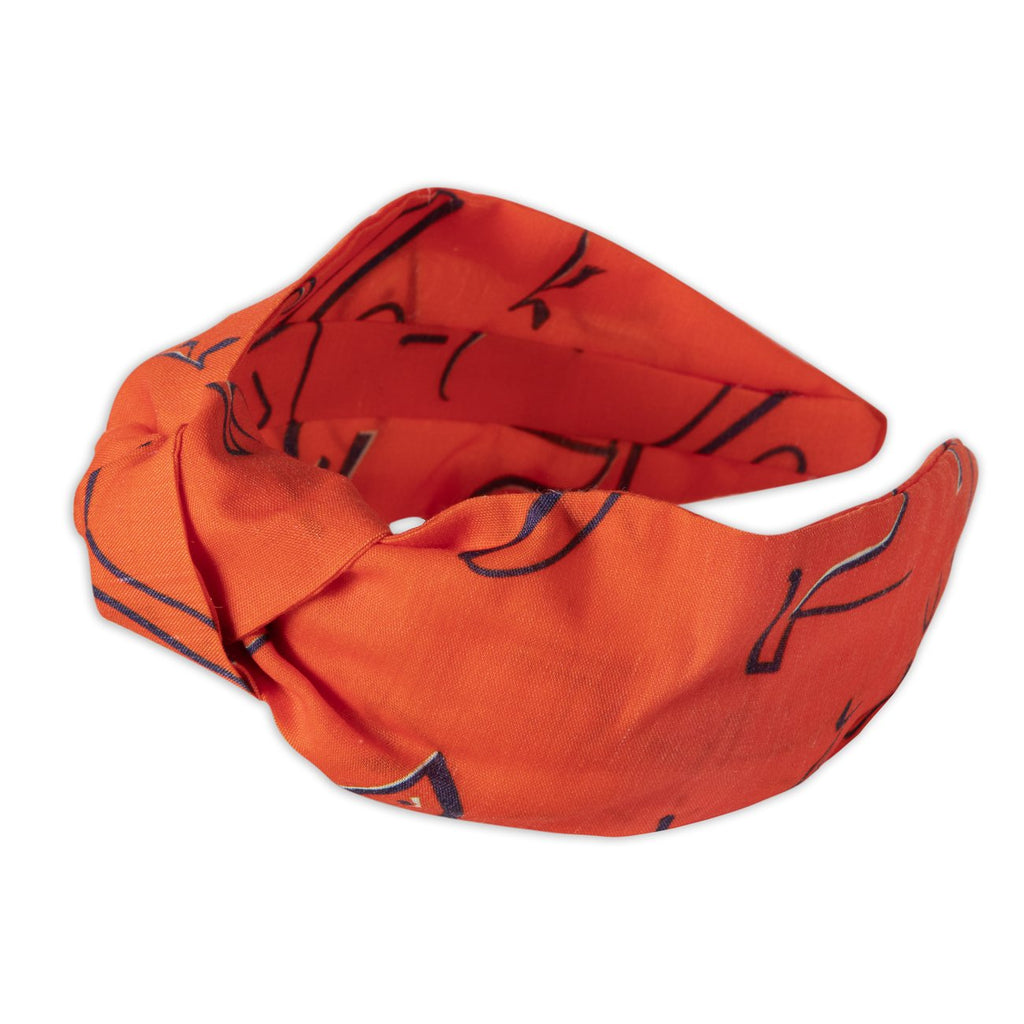 A Kate Whyley wide, knotted headband in tangerine orange, with black and white caligraphy-like design